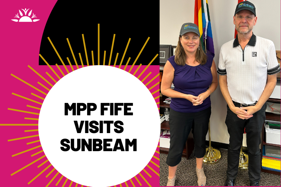 MPP Fife Visits Sunbeam! Photo of Sunbeam CEO Brian Swainson and MPP Catherine Fife with Sunbeam caps on standing in front of two flags.