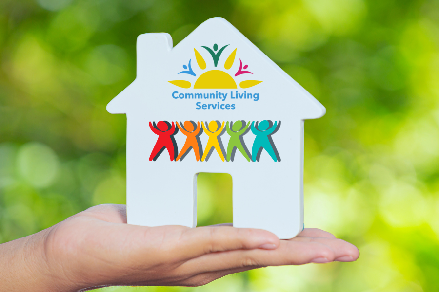 Hand holding ceramic white house with Sunbeam Community Living Services logo and silhouette of five people in rainbow colours